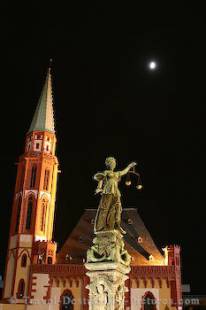 The statue of Justitia and a church at night in downtown Frankfurt, Germany.